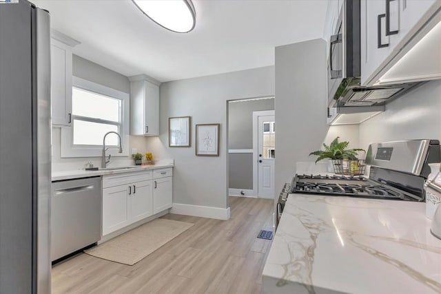 kitchen with light stone counters, stainless steel appliances, light wood-type flooring, white cabinets, and sink