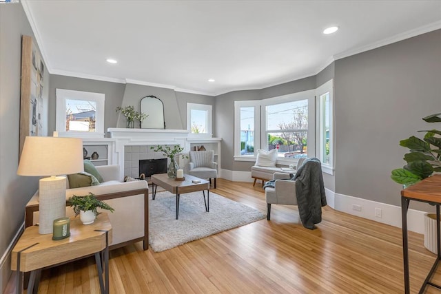 living room with a tile fireplace, ornamental molding, and light wood-type flooring