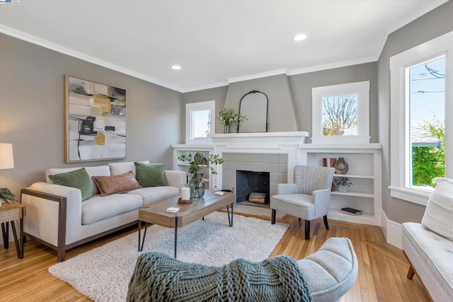 living room featuring ornamental molding, a tiled fireplace, and light hardwood / wood-style floors