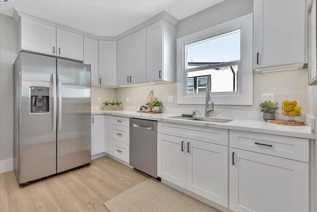 kitchen with appliances with stainless steel finishes, light wood-type flooring, white cabinets, and sink