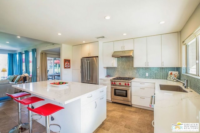 kitchen featuring white cabinets, a center island, sink, backsplash, and premium appliances