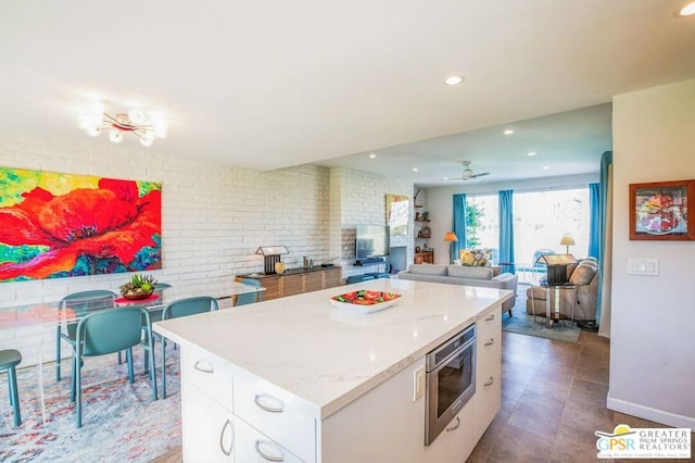 kitchen with ceiling fan with notable chandelier, a center island, brick wall, and white cabinetry