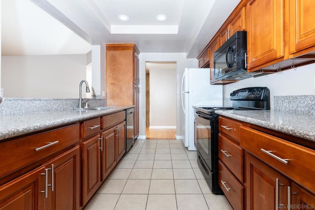 kitchen featuring light stone countertops, a raised ceiling, light tile patterned floors, black appliances, and sink