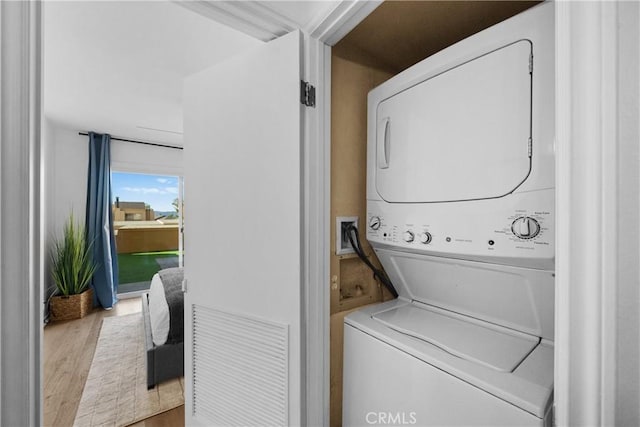 clothes washing area with stacked washer / drying machine and wood-type flooring