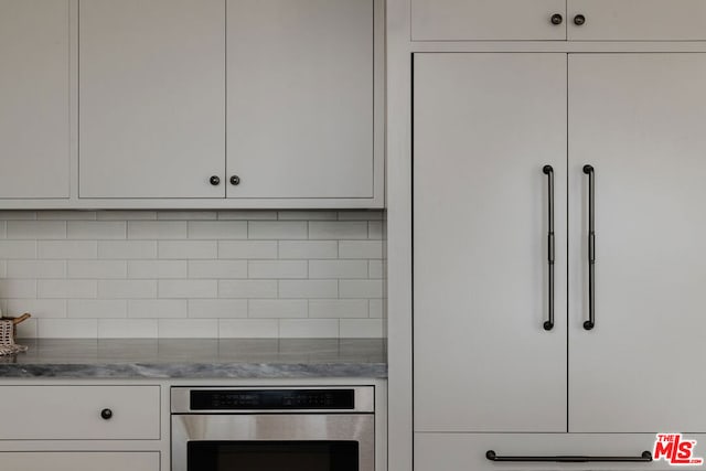 kitchen with stainless steel oven, light stone countertops, white cabinets, and decorative backsplash