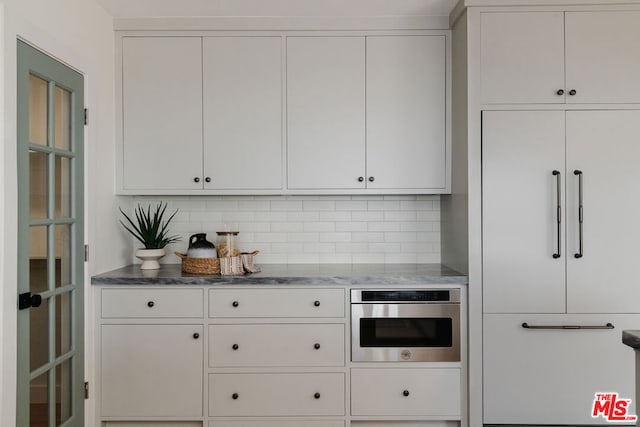 kitchen featuring light stone counters, stainless steel oven, backsplash, and white cabinetry