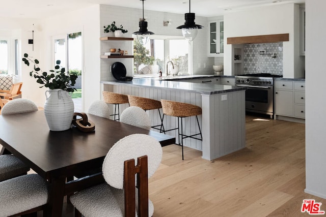 kitchen with white cabinetry, high end stainless steel range oven, a kitchen bar, kitchen peninsula, and hanging light fixtures