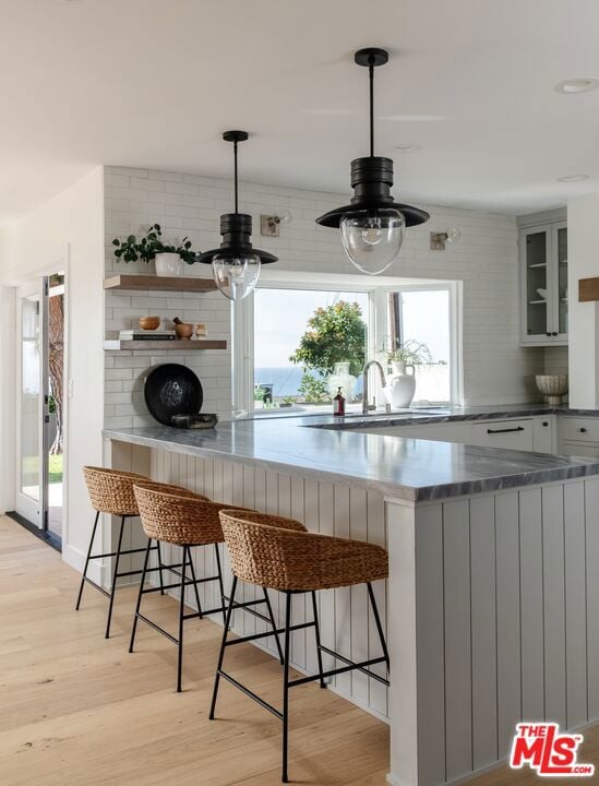 bar featuring sink, light hardwood / wood-style flooring, pendant lighting, and decorative backsplash