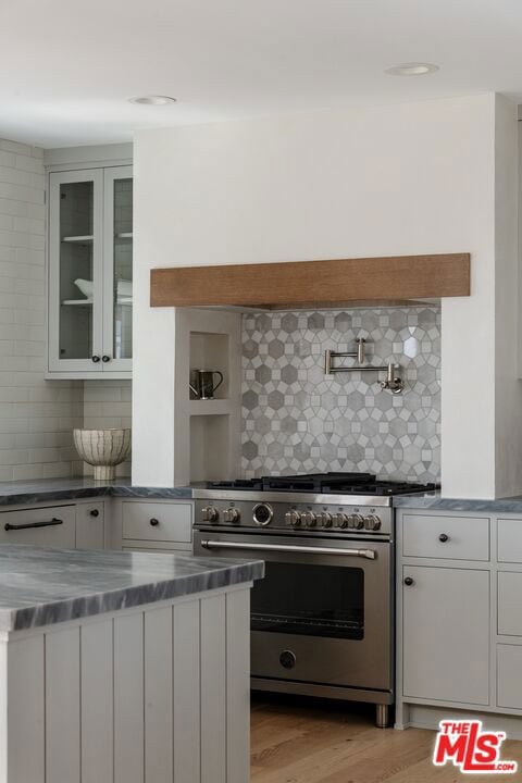 kitchen with light wood-type flooring, backsplash, high end stainless steel range, white cabinets, and stainless steel counters