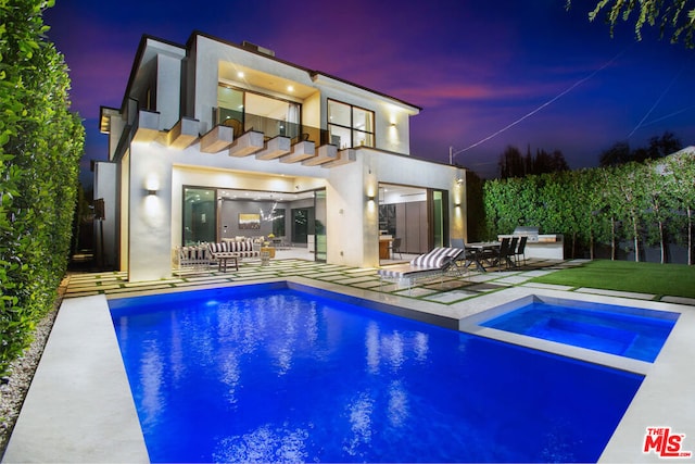 back house at dusk with a pool with hot tub, a balcony, and a patio