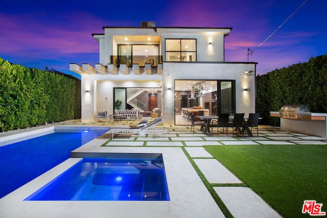 back house at dusk featuring an outdoor kitchen and a patio area