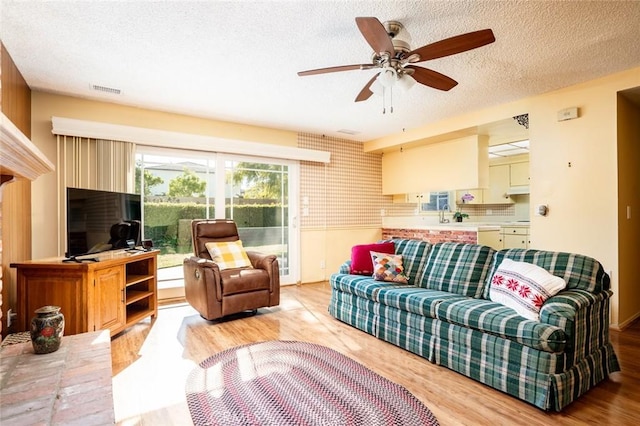 living room featuring a textured ceiling, ceiling fan, and light hardwood / wood-style flooring