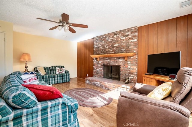 living room featuring a brick fireplace, a textured ceiling, ceiling fan, and light hardwood / wood-style flooring