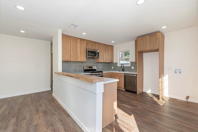 kitchen with sink, stainless steel appliances, dark hardwood / wood-style floors, decorative backsplash, and kitchen peninsula