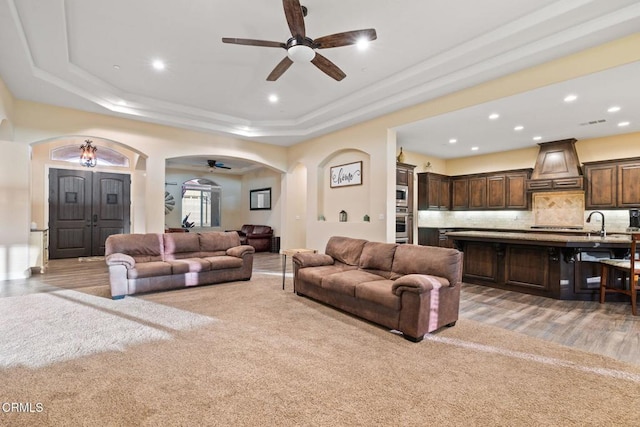 living room featuring ceiling fan, light colored carpet, and a raised ceiling