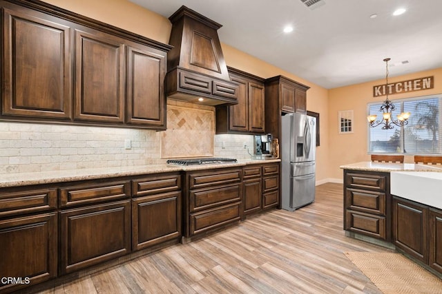 kitchen featuring light stone countertops, light hardwood / wood-style flooring, pendant lighting, stainless steel appliances, and a notable chandelier