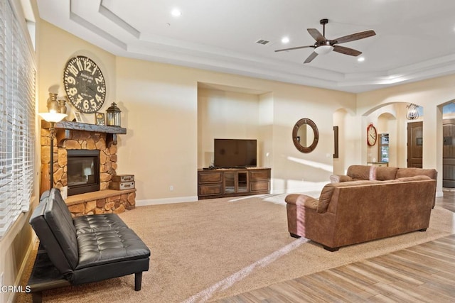 living room with a fireplace, a raised ceiling, and ceiling fan