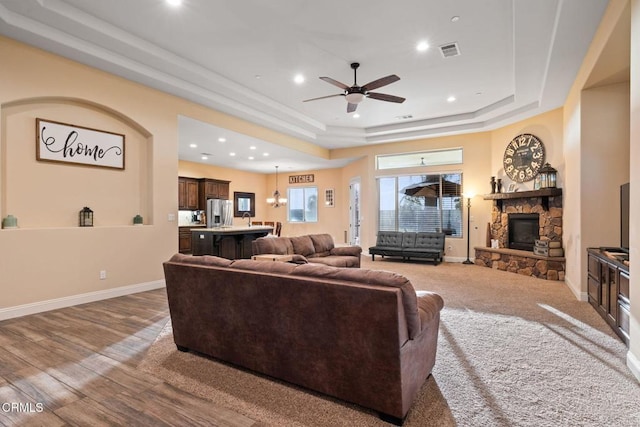 living room with hardwood / wood-style flooring, a raised ceiling, ceiling fan, and a stone fireplace