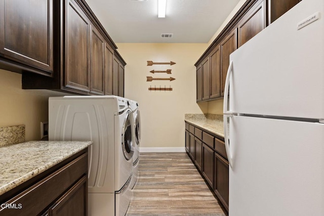 clothes washing area featuring washer and clothes dryer, light wood-type flooring, and cabinets