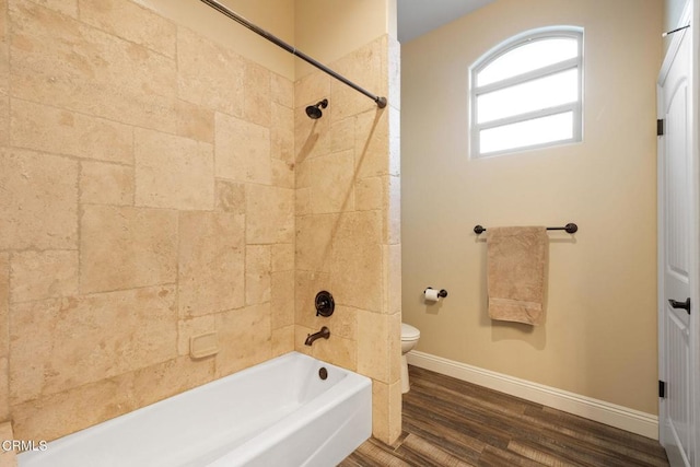 bathroom with hardwood / wood-style flooring, tiled shower / bath combo, and toilet