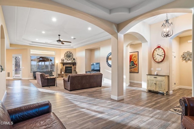 living room with ceiling fan with notable chandelier, a fireplace, a raised ceiling, and light hardwood / wood-style flooring