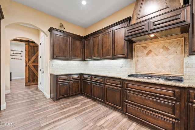 kitchen featuring stainless steel gas stovetop, backsplash, a barn door, and premium range hood