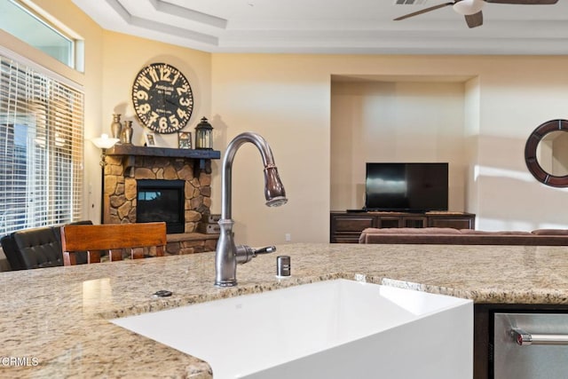 kitchen featuring sink, a fireplace, ceiling fan, and light stone countertops