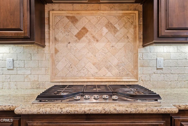 kitchen featuring light stone counters, dark brown cabinets, stainless steel gas cooktop, and tasteful backsplash