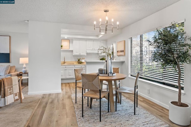 dining room with an inviting chandelier, light hardwood / wood-style flooring, a textured ceiling, and sink