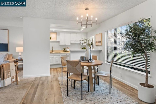 dining area with sink, an inviting chandelier, a textured ceiling, and light hardwood / wood-style floors