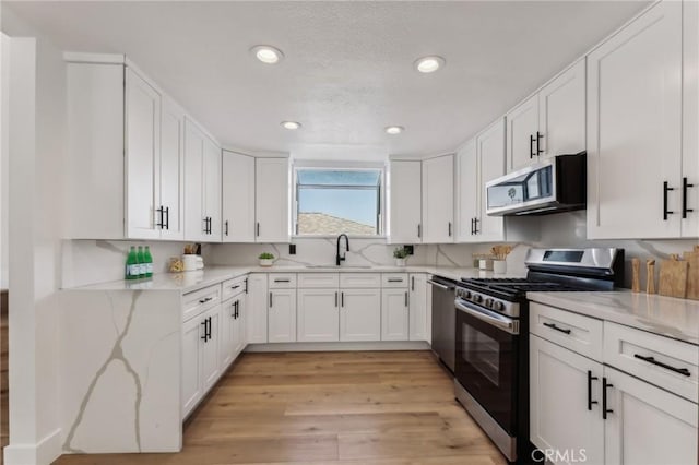 kitchen featuring sink, light hardwood / wood-style flooring, light stone countertops, appliances with stainless steel finishes, and white cabinets