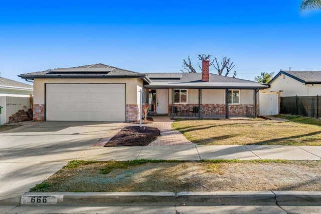 single story home with a porch, solar panels, a front yard, and a garage