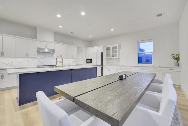 kitchen featuring light hardwood / wood-style flooring, a spacious island, a kitchen bar, white cabinets, and white refrigerator