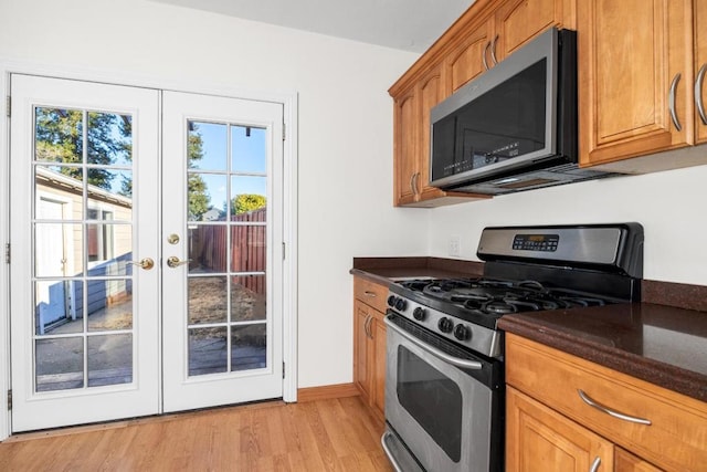 kitchen with appliances with stainless steel finishes, french doors, dark stone counters, and light hardwood / wood-style floors