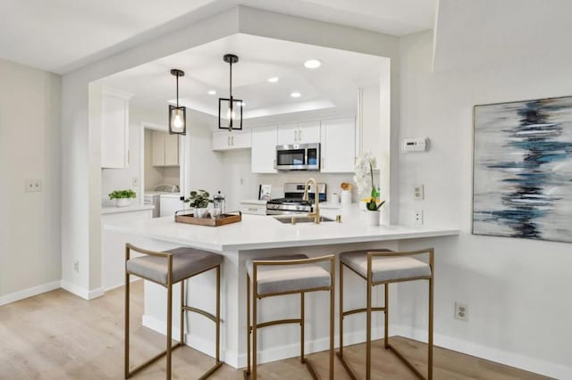 kitchen featuring decorative light fixtures, a raised ceiling, white cabinets, stainless steel appliances, and washer and clothes dryer