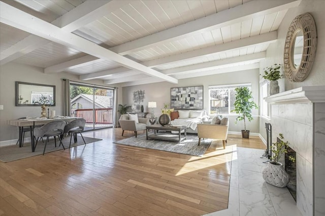 living room featuring beamed ceiling, a fireplace, and light wood-type flooring