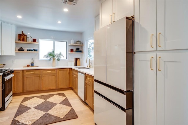 kitchen with gas stove, light hardwood / wood-style floors, stainless steel dishwasher, sink, and white cabinetry