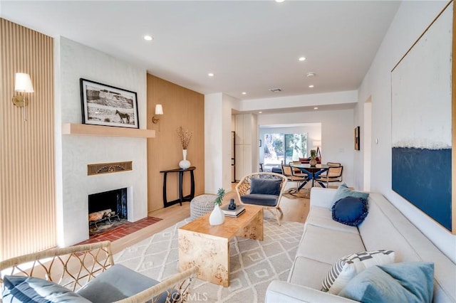 living room with light hardwood / wood-style floors, a large fireplace, and wooden walls