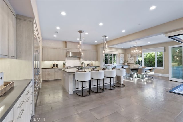 kitchen with decorative light fixtures, a center island with sink, an inviting chandelier, stainless steel gas stovetop, and a kitchen breakfast bar