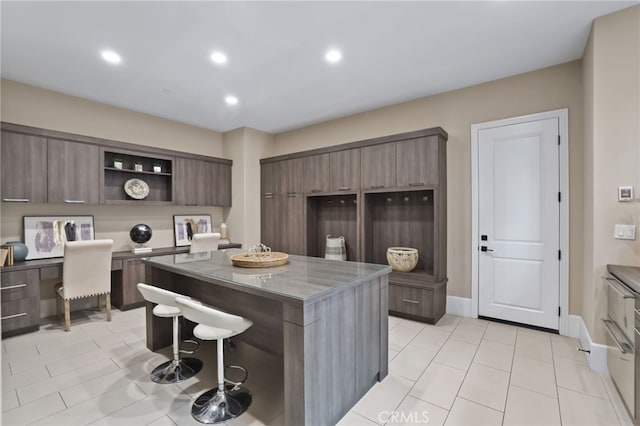 kitchen with a kitchen breakfast bar, a center island, light tile patterned flooring, and dark brown cabinetry