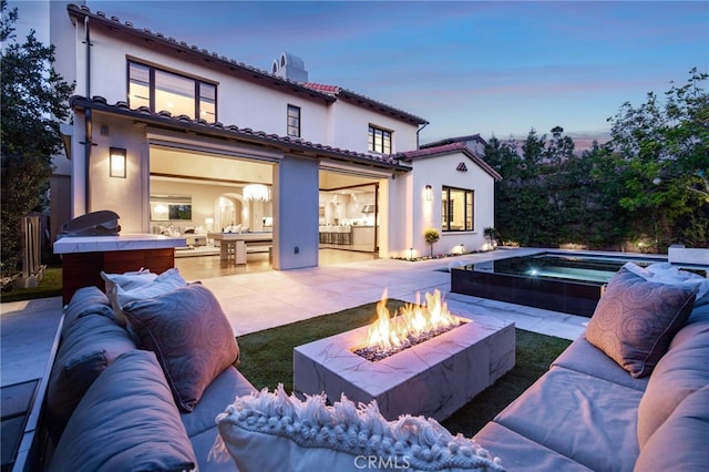 back house at dusk featuring an outdoor living space with a fire pit and a patio