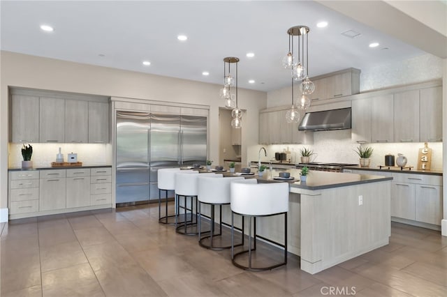 kitchen featuring stainless steel built in fridge, hanging light fixtures, a kitchen island with sink, a breakfast bar area, and sink