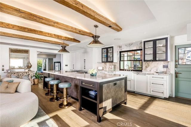 kitchen featuring hanging light fixtures, beamed ceiling, light stone counters, a kitchen island, and white cabinetry