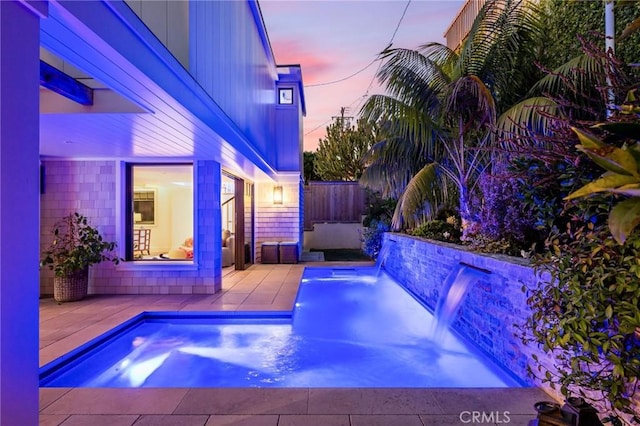 pool at dusk with a patio and pool water feature