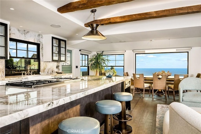 kitchen with a water view, light stone countertops, dark wood-type flooring, decorative backsplash, and beam ceiling