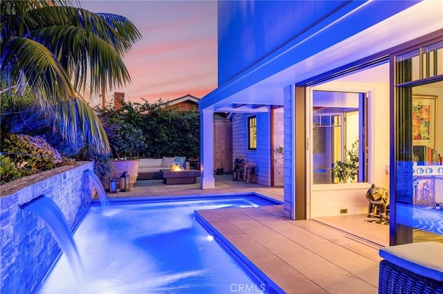 pool at dusk featuring an outdoor living space with a fire pit, pool water feature, and a patio area