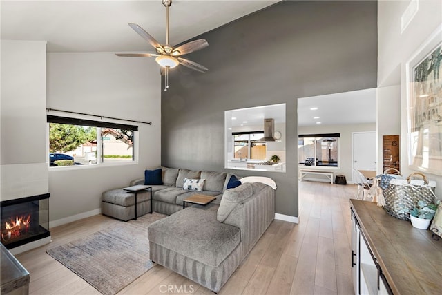 living room featuring a high ceiling, ceiling fan, and light hardwood / wood-style floors