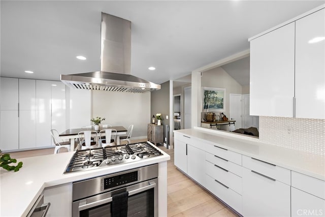 kitchen featuring appliances with stainless steel finishes, white cabinetry, backsplash, and island range hood