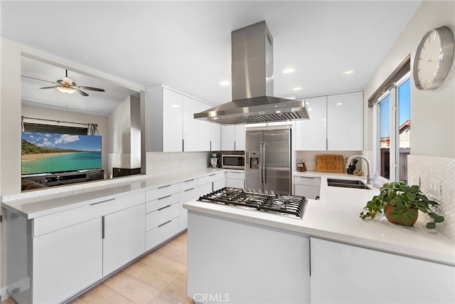 kitchen with kitchen peninsula, island exhaust hood, white cabinetry, appliances with stainless steel finishes, and sink