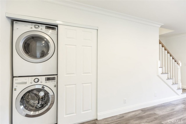 washroom with crown molding, stacked washer and clothes dryer, and light hardwood / wood-style flooring